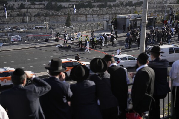 FILE - People look at Israeli police officers and volunteers from the Zaka rescue service work at the shooting attack in Jerusalem, Thursday, Nov. 30, 2023. The shooting death of an Israeli man who raced to confront Palestinian attackers has raised questions about the use of excessive force among Israeli security forces and the public. The man's shooting mirrors previous incidents where Israeli security forces or civilians have opened fire on attackers who no longer appear to pose a threat or on suspected assailants or unarmed civilians. (APPhoto/Ohad Zwigenberg, File)