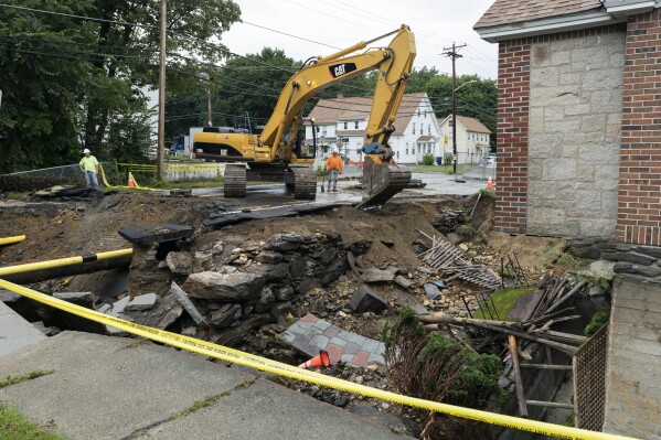 A sidewalk is removed by an excavator in front of a home where the front yard and road were washed away by recent flooding, Wednesday, Sept. 13, 2023, in Leominster, Mass. (AP Photo/Robert F. Bukaty)