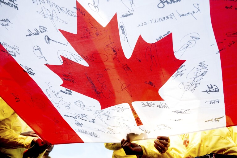 A South African firefighter holds a flag, gifted by Canadian firefighters as thanks for their work, as fellow crew members sign it Fox Creek, Alberta, on Tuesday, July 4, 2023. (AP Photo/Noah Berger)