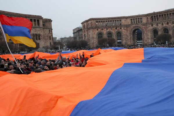 A crowd holds a huge Armenian national flag during a rally of supporters of Armenian Prime Minister Nikol Pashinyan in the center of Yerevan, Armenia, Monday, March 1, 2021. Amid escalating political tensions in Armenia, supporters of the country's embattled prime minister and the opposition are staging massive rival rallies in the capital of Yerevan. Prime Minister Nikol Pashinyan has faced opposition demands to resign since he signed a peace deal in November that ended six weeks of intense fighting with Azerbaijan over the Nagorno-Karabakh region. (Hayk Baghdasaryan/PHOTOLURE via AP)
