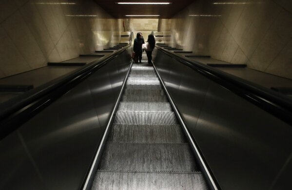 Two people stand in an empty staircase leading to the subway, in Milan, northern Italy, Wednesday, Feb. 26, 2020. Italy has been struggling to contain the rapidly spreading outbreak that has given the country more coronavirus cases outside Asia than anywhere else.  (AP Photo/Antonio Calanni)