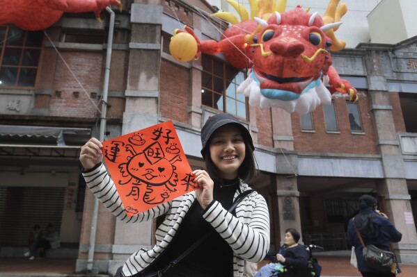 A woman holds a spring couplet with dragon patterns that she drew herself for the upcoming Lunar New Year celebrations at the Dihua street market in Taipei, Taiwan, Thursday, Feb. 8, 2024. Taiwanese shoppers started hunting for delicacies, dried goods and other bargains at the market ahead of the Lunar New Year celebrations which fall on Feb. 10 this year. (APPhoto/Chiang Ying-ying)