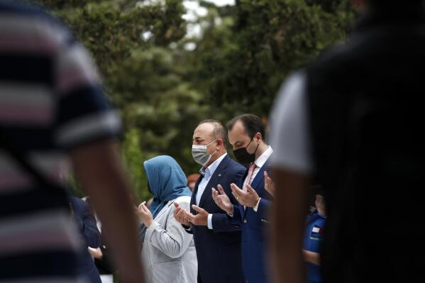 Turkish Foreign Minister Mevlut Cavusoglu, center, prays over the grave of Ahmet Sadik, who was an MP at the Greek parliament, at a muslim cemetery at Komotini town, in northeastern Greece, Sunday, May 30, 2021. Greece's prime minister said Friday his country is seeking improved ties with neighbor and longtime foe Turkey, but that the onus is on Turkey to refrain from what he called "provocations, illegal actions and aggressive rhetoric." (AP Photo/Giannis Papanikos)