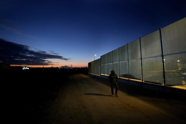 FILE - A man walks by the fence at the Pournara migrant reception center in Kokkinotrimithia outside of capital Nicosia, Cyprus, on Jan. 24, 2024. Cyprus says it’s suspending processing all asylum applications by Syrian nationals because of large numbers of refugees from the war-torn country that continue to reach the island nation by boat, primarily from Lebanon. (AP Photo/Petros Karadjias, File)