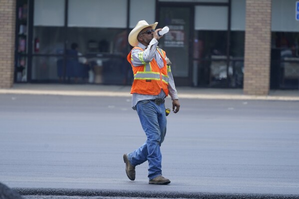 Rudy Gasca drinks water during a parking lot asphalt resurfacing job in Richardson, Texas, Tuesday, June 20, 2023. (AP Photo/LM Otero)