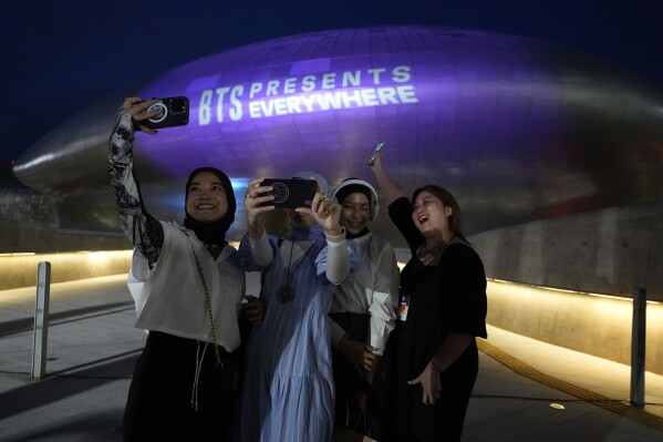 The landmark Dongdaemun Design Plaza is illuminated in purple as fans take a selfie in Seoul, South Korea, Monday, June 12, 2023. Skyscrapers, bridges and other landmarks in South Korea's capital will be lit up in purple on Monday as the country begins celebrating the 10th anniversary of K-pop band BTS, whose global popularity is a source of national pride. (AP Photo/Ahn Young-joon)