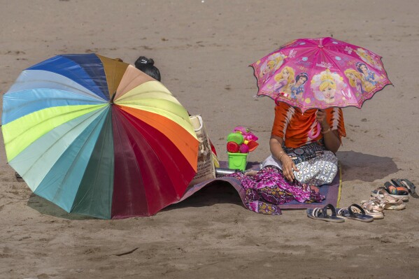 Women sit in Juhu beach holding umbrellas to protect themselves from the sun on a hot summer day in Mumbai, India, Thursday, May 2, 2024. (Ǻ Photo/Rafiq Maqbool)