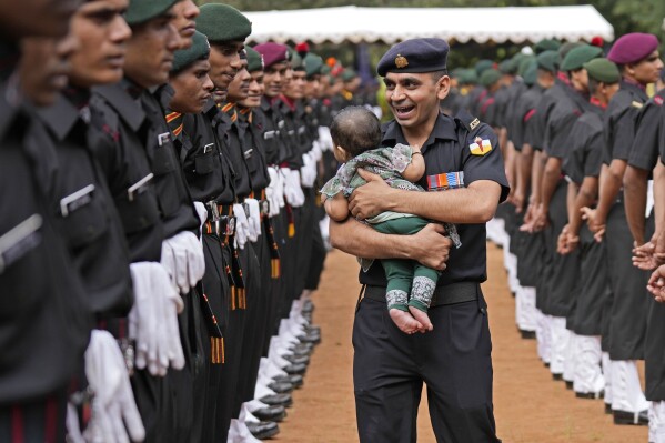 An Indian Army soldier carries his child and walks past graduating soldiers from the first batch of Agniveer scheme during their graduation ceremony in Bengaluru, India, Friday, Aug. 4, 2023. (AP Photo/Aijaz Rahi)