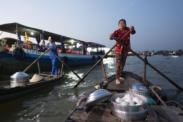 With the lid of her steamer off, Nguyen Thi Thuy, a vendor selling buns, rushes to a passing tourist boat past another bun vendor on a floating market in Can Tho, Vietnam, Wednesday, Jan. 17, 2024. (AP Photo/Jae C. Hong)