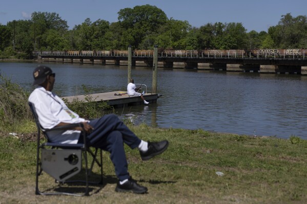 Bruce Holmes observes a train passing over the Anacosita River on Wednesday, May 1, 2024, at Anacostia Park in Washington. Bruce, a native resident of Washington, D.C., teaches kids in the area about fishing along the Anacostia River. (AP Photo/Tom Brenner)