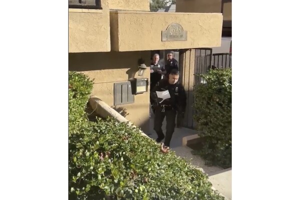 In this frame grab taken from video provided by attorney Dermot Givens, Los Angeles Police Department officers approach Givens with a copy of a search warrant outside his home, in Los Angeles, Tuesday, Jan. 23, 2024. A Los Angeles judge has ordered the city’s police department to return or destroy photographs of legal documents that were allegedly taken by officers during the unannounced raid on the home of Givens, who represents a prominent Black Lives Matter activist. (Dermot Givens via AP)