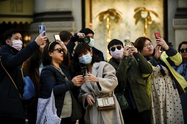 People, some wearing sanitary masks, take photos in central Milan, Italy, Monday, Feb. 24, 2020. At least 190 people in Italy’s north have tested positive for the COVID-19 virus and four people have died, including an 84-year-old man who died overnight in Bergamo, the Lombardy regional government reported. (Claudio Furlan/Lapresse via AP)