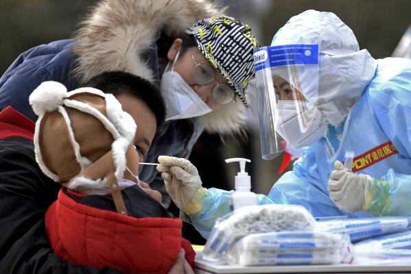 In this photo released by Xinhua News Agency, a medical staff in a protective suit takes a swab from a child near a residential area in Shijiazhuang in northern China's Hebei Province on Sunday, Jan. 10, 2021. Chinese health authorities say scores more people have tested positive for coronavirus in Hebei province bordering on the capital Beijing. The outbreak focused on the Hebei cities of Shijiazhuang and Xingtai is one of China's most serious in recent months and comes amid measures to curb the further spread during next month's Lunar New Year holiday. (Wang Xiao/Xinhua via AP)