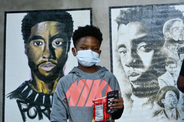 A boy stands in front of two paintings of Chadwick Boseman during the opening of an art exhibit honoring the actor in his hometown of Anderson, S.C. on Thursday, Oct. 22, 2020. Nearly 20 local artists took part in the city sponsored project. (Charles McBryde, Via AP)