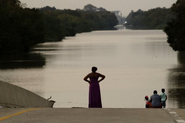FILE - In this Friday, Sept. 1, 2017 file photo, Jessica Anderson, with her husband Darrell and daughters Lauren, and Harper look at floodwaters in Addicks Reservoir from a closed freeway in the aftermath of Hurricane Harvey in Houston. October 2020's Hurricane Delta, gaining strength as it bears down on the U.S. Gulf Coast, is the latest and nastiest in a recent flurry of rapidly intensifying Atlantic hurricanes that scientists largely blame on global warming. (AP Photo/Charlie Riedel)