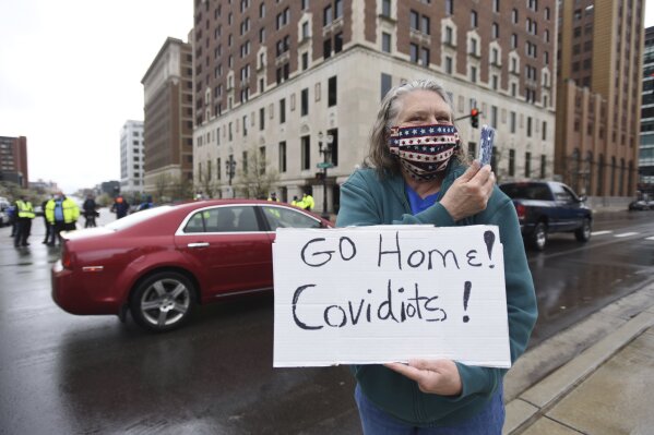 Karen Spitler of Lansing , an counter-protesters holds a sign during a rally at the state Capitol in Lansing, Mich., Thursday, April 30, 2020. Hoisting American flags and handmade signs, protesters returned to the state Capitol to denounce Gov. Gretchen Whitmer's stay-home order and business restrictions due to COVID-19, while lawmakers met to consider extending her emergency declaration hours before it expires. (Matthew Dae Smith/Lansing State Journal via AP)