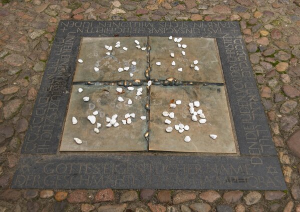 In this Tuesday, Jan. 14, 2020 photo stones are dropped at a commemorative plaque besides the Stadtkirche (Town Church) in Wittenberg, Germany. The church contains a so-called “Judensau,” or “Jew pig,” sculpture which is located about 4 meters, 13 feet, above the ground on a corner of the church. A court in eastern Germany will consider next week a Jewish man’s bid to force the removal of an ugly remnant of centuries of anti-Semitism from a church where Martin Luther once preached. (AP Photo/Jens Meyer)