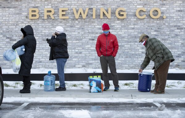 Tina Hall, left to right, Susana Sosa, Jim Sefcik and Chris Sosa wait in line to fill up their containers with water at Meanwhile Brewing Company in Austin, Texas, on Friday, Feb. 19, 2021, during a citywide boil water notice caused by the winter storm. The brewery gave away all 4,000 gallons of their water to people in need on Thursday and Friday. (Jay Janner /Austin American-Statesman via AP)