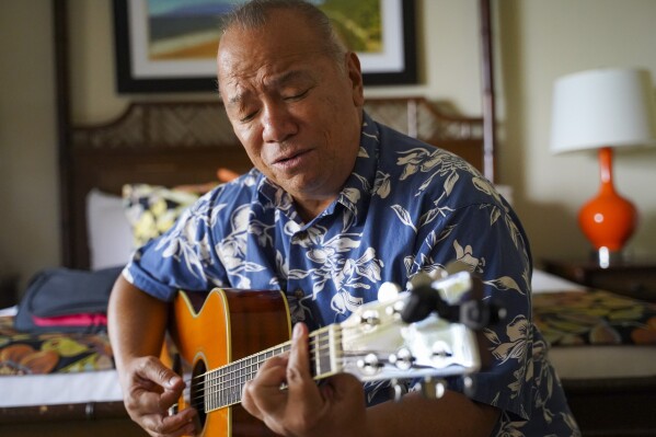 Charles Nahale plays the only guitar he took with him from the wildfire on Tuesday, Oct. 10, 2023, in Lahaina, Hawaii. Nahale had many guitar and ukulele collections that were burned down in his home on Front Street. (AP Photo/Mengshin Lin)