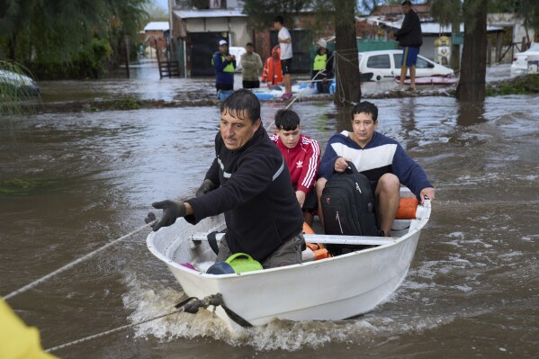 A man pulls on a rope to glide a a boat carrying residents across a flooded street after heavy rains in Campana, Argentina, Saturday, May 17, 2025. (AP Photo/Rodrigo Abd)