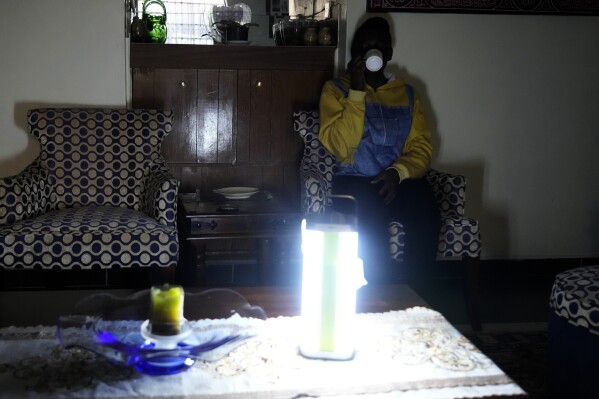 A Kenyan sips a cup of tea as she sits in her sitting room with emergency light as there was no electricity Saturday, Aug. 26 2023. Much of Kenya remains without electricity Saturday morning after an unexplained power outage Friday night shut down the country's main international airport and led to a rare public apology by a government minister.(AP Photo/Abdul Azim Sayyid)