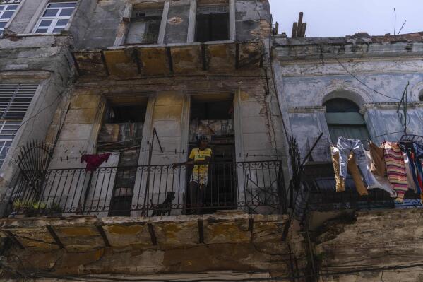 Anet Ayala and her dog peer from her balcony in Havana, Cuba, Monday, June 13, 2022. Ayala and her brother filled out paperwork to get authorization to legally fix their home, which dates to the 20th century, but the building permit, mandatory in Cuba, was never delivered. (AP Photo/Ramon Espinosa)