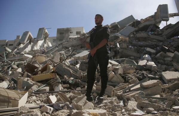 A policeman stands on rubble from a building housing AP office and other media in Gaza City that was destroyed after Israeli warplanes demolished it, Saturday, May 15, 2021.  The airstrike Saturday came roughly an hour after the Israeli military ordered people to evacuate the building. There was no immediate explanation for why the building was targeted. (AP Photo/Hatem Moussa)