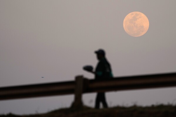 A Supermoon is seen on the sky as a woman walks on the street, in Vosloorus, east of Johannesburg, South Africa, Wednesday, Aug. 30, 2023. August 30 sees the month's second supermoon, when a full moon appears a little bigger and brighter thanks to its slightly closer position to Earth. (AP Photo/Themba Hadebe)