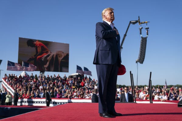 ARCHIVO - El expresidente Donald Trump de pie mientras suena la canción "Justicia para todos" durante un mitin de campaña en el Aeropuerto Regional de Waco, el 25 de marzo de 2023, en Waco, Texas. La canción presenta a un coro de hombres encarcelados por su papel en la insurrección del 6 de enero de 2021 en el Capitolio de los EE. UU. cantando el himno nacional y una grabación de Trump recitando el juramento a la bandera. (Foto AP/Evan Vucci)