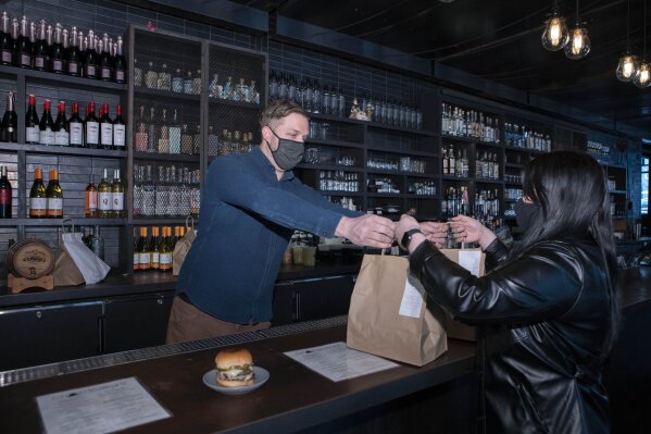 Josh Phillips, the co-owner of Espita, a stylish Mexican restaurant, hands over carryout to a customer at his restaurant in downtown Washington, Monday, Feb. 15, 2021. Phillips opened a delivery-only brand called Ghostburger in August to keep Espita’s kitchen running through the winter. He chose burgers because he wanted to reach new customers at a lower price point than Espita. It’s been so successful that Phillips is now scouting for locations for standalone Ghostburger restaurants. (AP Photo/Jose Luis Magana)