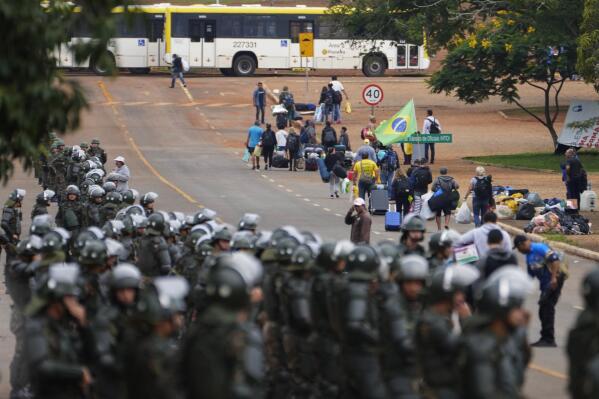 Police officers take position as supporters of Brazil's former President Jair Bolsonaro leave a camp outside the Army headquarters in Brasilia, Brazil, Monday, Jan. 9, 2023. Since Bolsonaro lost re-election to Luiz Inácio Lula da Silva on Oct. 30, his supporters have gathered across the country refusing to concede defeat and asking for the armed forces to intervene. (AP Photo/Eraldo Peres)