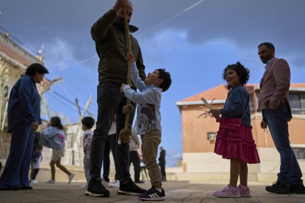 A boy rings the bell of the Maronite Church of St. George as his sister holds a candle during the traditional Palm Sunday procession in Quraye, near the southern port city of Sidon, Lebanon, Sunday, April 13, 2025. (AP Photo/Hassan Ammar)