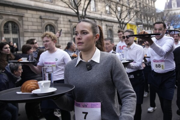 Waiters carry trays with a cup of coffee, a croissant and a glass of water as they take part in a waiter's run through the streets of Paris, Sunday, March 24, 2024. (AP Photo/Christophe Ena)