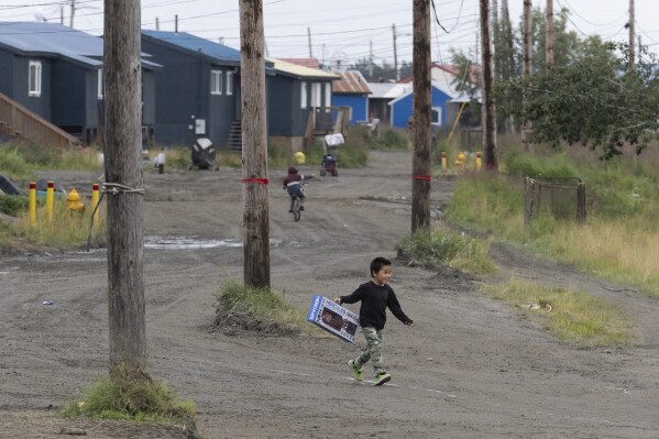 A child crosses Main Street while carrying a Hercules toy from the Akiachak Enterprises general store, Friday, Aug. 18, 2023, in Akiachak, Alaska. (AP Photo/Tom Brenner)