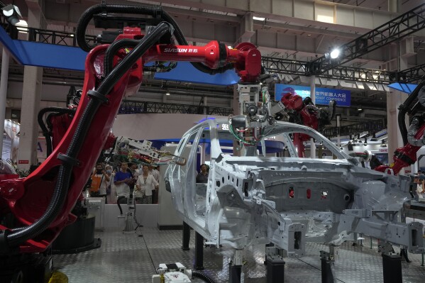 FILE - Visitors look at the robotic arms assembly a vehicle frame during the annual World Robot Conference at the Etrong International Exhibition and Convention Center in the outskirt of Beijing, Thursday, Aug. 17, 2023. China's factories picked up their pace and retail sales also gained momentum in August, the government reported Friday, Sept. 15, 2023, suggesting the economy may be gradually recovering from its post-pandemic malaise. (AP Photo/Andy Wong, File)