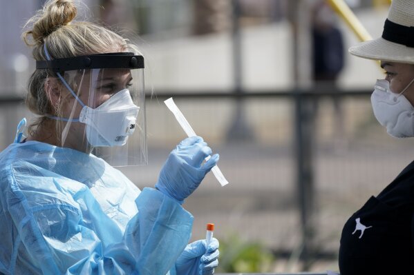 FILE - In this Aug. 13, 2020, file photo, nurse practitioner Debbi Hinderliter, left, collects a sample from a woman at a coronavirus testing site near the nation's busiest pedestrian border crossing in San Diego. The credibility of two top public health agencies is on the line after controversial decisions that outside experts say suggest political pressure from the Trump administration. The Centers for Disease Control and Prevention triggered a backlash from the medical community by rewriting its guidelines to recommend less testing. (AP Photo/Gregory Bull, File)