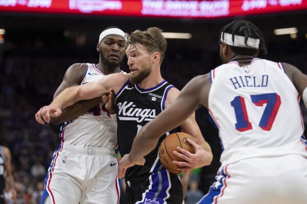 Sacramento Kings forward Domantas Sabonis (10) drives to the basket as Philadelphia 76ers forward Paul Reed (44) and guard Buddy Hield (17) defend in the second half of an NBA basketball game in Sacramento, Calif., Monday, March 25, 2024. The Kings won 108-96. (AP Photo/José Luis Villegas)