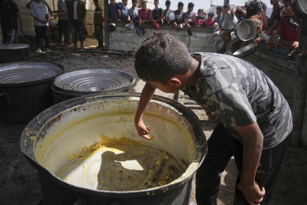 A boy scrapes leftovers from an empty pot after all the meals were distributed at a community kitchen in Khan Younis, southern Gaza Strip, Wednesday, May 14, 2025. (AP Photo/Abdel Kareem Hana)