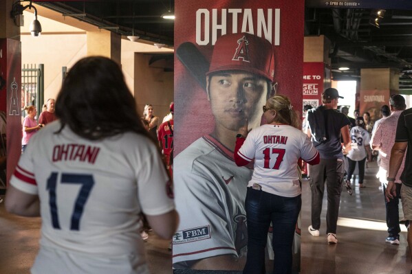 A fan poses for photos with a display showing the image of Los Angeles Angels' Shohei Ohtani before the team's baseball game against the Texas Rangers on Wednesday, Sept. 27, 2023, in Anaheim, Calif. (AP Photo/Jae C. Hong)