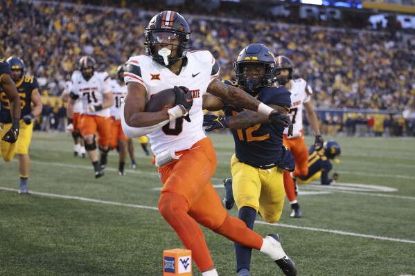 Oklahoma State's Ollie Gordon (0) carries the ball in for a rushing touchdown as West Virginia's Anthony Wilson (12) pursues during the second half of an NCAA college football game Saturday, Oct. 21, 2023, in Morgantown, W.Va. (AP Photo/Chris Jackson)