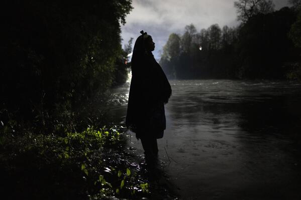 Millaray Huichalaf, a Mapuche machi, or healer and spiritual guide, poses for a portrait in the Pilmaiquen River silhouetted by lights from the construction site of a hydroelectric plant in Carimallin, southern Chile, on Monday, June 27, 2022. Huichalaf has led a sometimes-violent battle against hydroelectric plants on the Pilmaiquen, which flows through rolling pastures from a lake in the Andean foothills. (AP Photo/Rodrigo Abd)