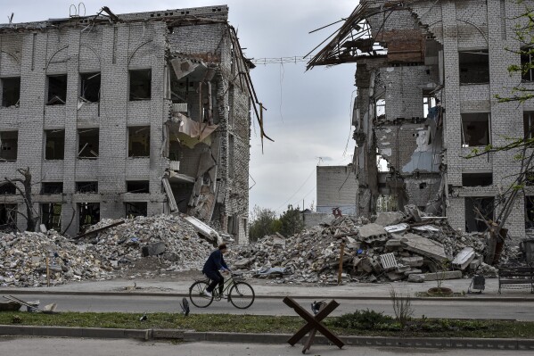 FILE – A local woman rides a bicycle on April 18, 2024, in front of a building destroyed by a Russian airstrike in the frontline town of Orikhiv, Ukraine.  House Speaker Mike Johnson, R-La., putting his position on the line, this week relied on Democratic support to bring to the House a series of votes on $95 billion in foreign aid to Ukraine, Israel and other US allies.  Since President Joe Biden made the funding request in October, the Republican-controlled House has consistently emerged as the biggest obstacle to final passage.  (AP Photo/Andriy Andriyenko)