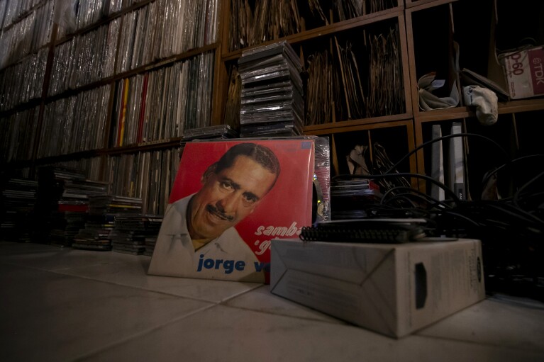 Jorge Veiga's 1963 Samba E Ginga album cover is propped against a shelf filled with Carlos Savalla's music collection, in his studio in Rio de Janeiro, Brazil, Friday, April 19, 2024. Savalla, a 66-year-old music producer in Rio, owns more than 60,000 vinyl records. (AP Photo/Bruna Prado)
