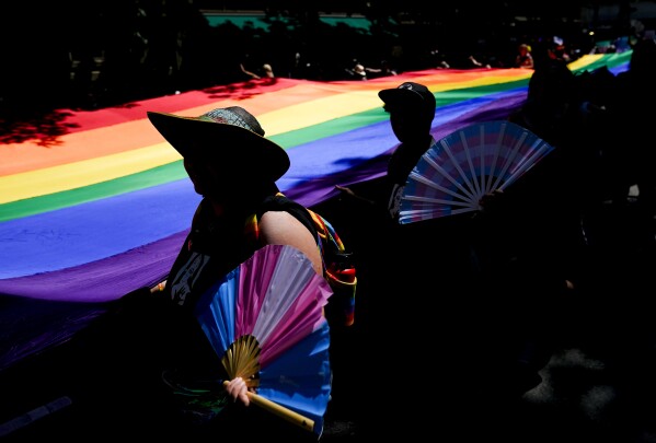 FILE - Mac Weatherill, left, and Yexara Colón Martinez, second from left, hold transgender pride fans as they help carry a large rainbow flag on their fourth anniversary during the annual Seattle Pride Parade, Sunday, June 25, 2023, in Seattle. (AP Photo/Lindsey Wasson, File)