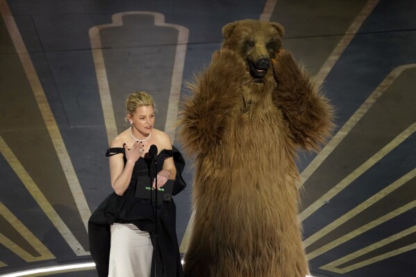 Elizabeth Banks, left, and an actor dressed in a costume from her movie "Cocaine Bear" present the award for best visual effects at the Oscars on Sunday, March 12, 2023, at the Dolby Theatre in Los Angeles. (AP Photo/Chris Pizzello)