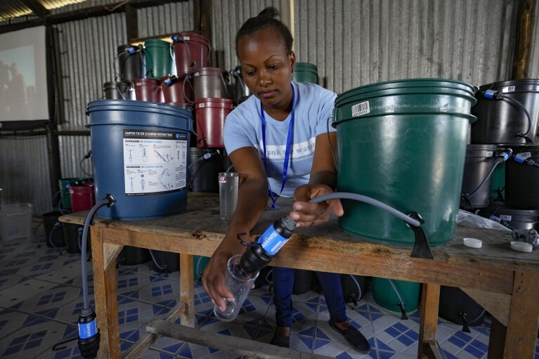 Hellen Simichi, a member of the Bucket Ministry, a Christian nonprofit organization, demonstrates how to use a bucket filter to locals in Athi River, Machakos county, Kenya, Tuesday, Oct. 17, 2023. (AP Photo/Brian Inganga)