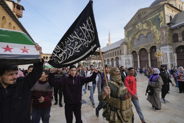 A masked opposition fighter carries a flag of Hayat Tahrir al-Sham (HTS) in the courtyard of the Umayyad Mosque in the old walled city of Damascus, Syria, on Tuesday, Dec. 10, 2024. HTS is the largest rebel faction within the opposition that toppled Bashar Assad's regime last Sunday. (AP Photo/Hussein Malla, File)