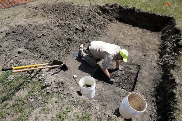 Nebraska State Archeologist Dave Williams clears soil away soil as workers dig for the suspected remains of children who once attended the Genoa Indian Industrial School, Monday, July 10, 2023, in Genoa, Neb. The mystery of where the bodies of more than 80 children are buried could be solved this week as archeologists dig in a Nebraska field that a century ago was part of a sprawling Native American boarding school. (AP Photo/Charlie Neibergall)