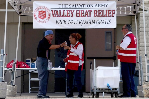 FILE - Salvation Army volunteer Francisca Corral, center, gives water to a man at a their Valley Heat Relief Station, July 11, 2023 in Phoenix. More Americans believe they've personally felt the impact of climate change because of recent extreme weather, including a summer that brought dangerous heat for much of the United States, according to new polling from The Associated Press-NORC Center for Public Affairs Research. (AP Photo/Matt York, File)
