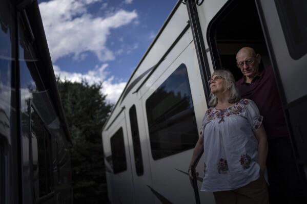 Sandy Phillips, left, and her husband, Lonnie, stand for a portrait in Longmont, Colo., Monday, Sept. 4, 2023. Suffering through their own personal loss after a mass shooting in Colorado in 2012, the couple set out to help other parents like them, traveling to shooting sites around the country in this RV. The trip continued for a decade. (AP Photo/David Goldman)